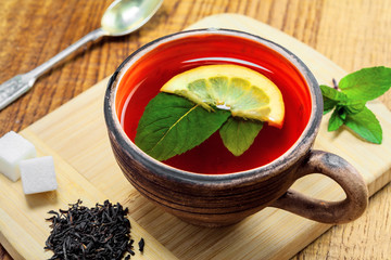 Healthy hot beverage in a rustic clay crockery. Black Ceylon tea with fresh mint leaves and lemon on a wooden table.