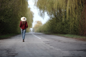 Beautiful woman walking back on asphalt road, goes, straw hat, outdoor with effect toning