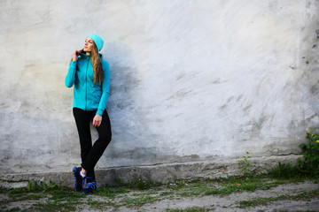 Beautiful girl in sports clothes stands near a gray relief wall, urban style