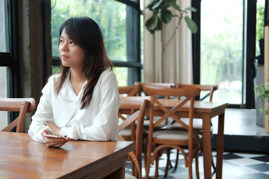 young women sitting at wooden table in morning and using mobile phone. she thinking and look like waiting for someone. image for business,people,technology,portrait and emotion concept