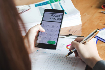 Woman with bills and smart phone at the table. Calculation of costs