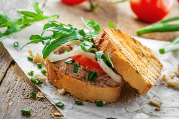 Sandwich made of grilled toasts, tuna salad, tomato, onion and arugula on a table. Delicious healthy meal for lunch.