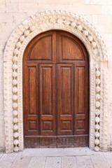 Antique wooden door framed by stucco ornaments in white wall