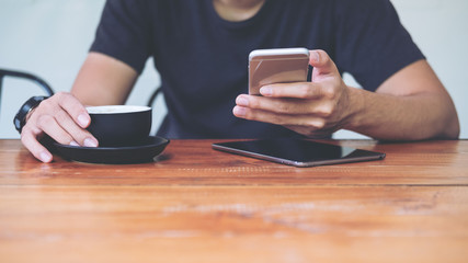 A man using smart phone and holding coffee cup in modern cafe