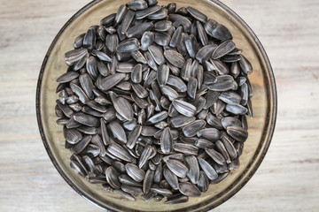 Black sunflower seeds in a black transparent plate on a light wooden background