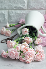 Small tender pink carnation flowers in enamel vase on gray concrete with copy space, mother's day greeting card background, vertical