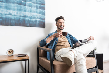 Cheerful youthful man taking pleasure from hot beverage at home