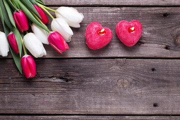Two red  burning candles in form of  heart  and bright tulips flowers on rustic wooden background