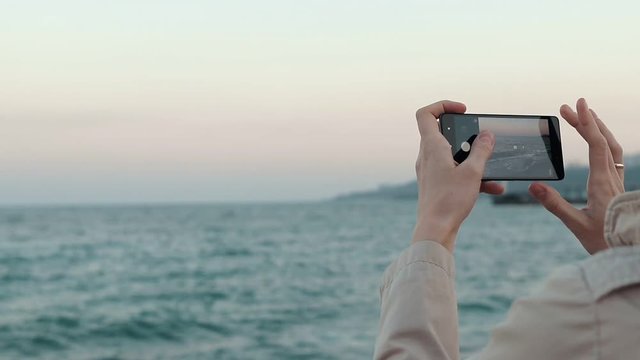 Close-up of a woman photographing an ocean on a mobile phone, slow motion