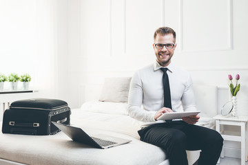 Businessman on bed working with a tablet and laptop from his hotel room