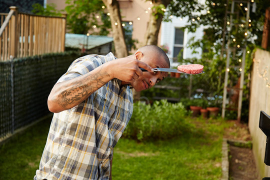 Mid adult man looking at raw burger in garden