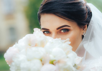 Naklejka premium A beautiful warrior bride with blue eyes looks at the camera hiding behind a bouquet of white flowers