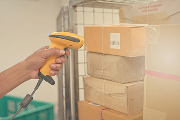 Postman worker scanning package with barcode scanner in warehouse for delivery.