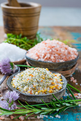 Three different types of natural salt in stone bowls on wooden surface. White sea salt, pink Himalayan salt, Spiced salt with rosemary