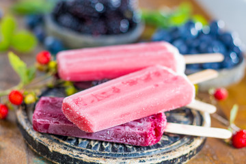 Fresh summer wild blueberries,  brambleberry, strawberry and home made sorbet ice cream popsicles on stone plate - obrazy, fototapety, plakaty
