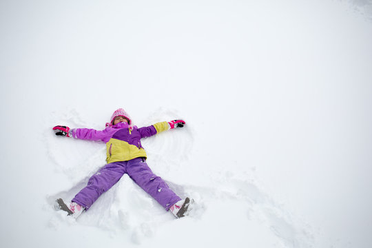 Young girl making snow angel in snow
