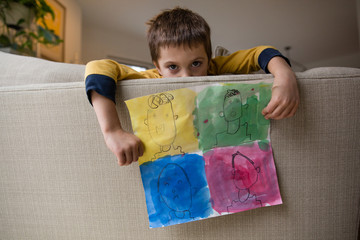 Young boy leaning over sofa, holding artwork, showing different emotions