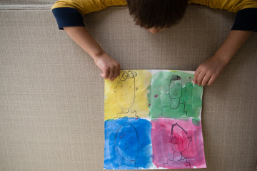 Young boy leaning over sofa, holding artwork, showing different emotions
