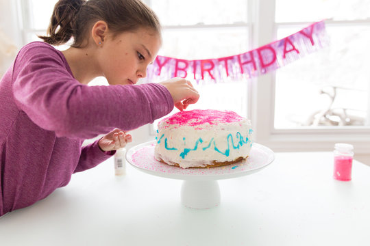 Girl decorating birthday cake with sprinkles
