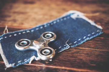 Top view image of a metal silver color fidget spinner on jean cloth with wooden table background