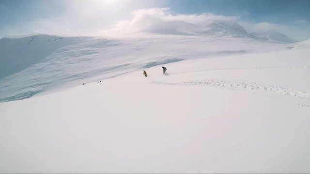 Man skier skiing down mountain with friends and waits in the middle of hill 