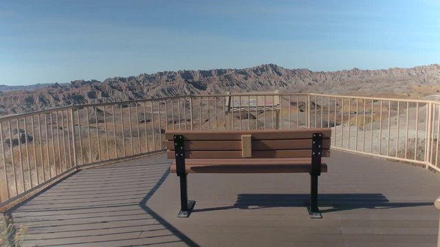 CLOSE UP: Empty bench with a view of sunny Badlands National park on a sunny day. Lonely bench at the end of a boardwalk overlooking stunning desert landscape and high pointy mountains in South Dakota
