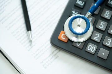 Close up of stethoscope on calculator and bill with pen.