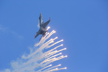 Modern jet fighter is firing a set of flares against a blue sky. Cloud condensation on the wings. White smoke trails and sparkling missiles.