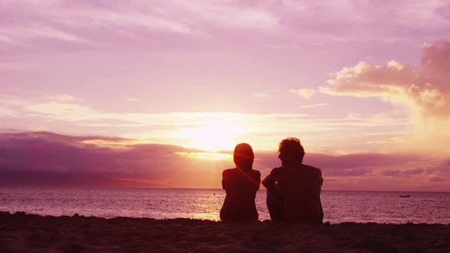 Romantic couple relaxing enjoying on beach looking at sunset with beautiful light and colors. Young couple on honeymoon enjoying travel vacation summer holidays on beach. SLOW MOTION RED EPIC.