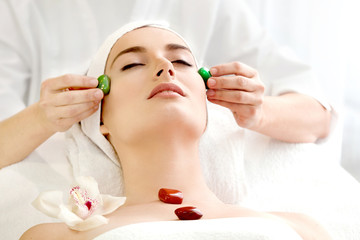 Spa salon: Young Beautiful Woman Having Facial Massage with Stones .