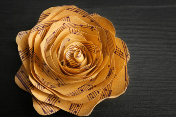 Beautiful rose made of music notes on wooden table closeup