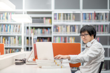 Young Asian university student working with laptop computer and notebook in library, self learning and college lifestyle concepts