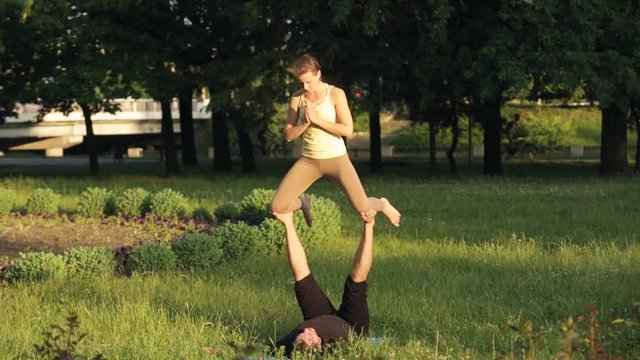 Amazing couple practicing acro yoga. Professional yoga instructors practice in a city park. Two successful young people perform acro yoga exercises. Man and a woman learn yoga at sunset.