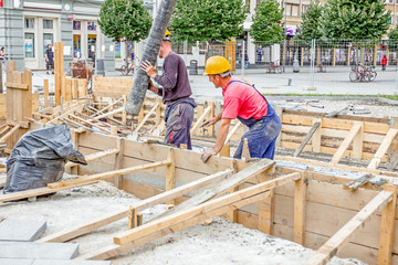 Fototapeta premium Workers are pouring fresh concrete in vertical wooden mold with hose, continuous casting