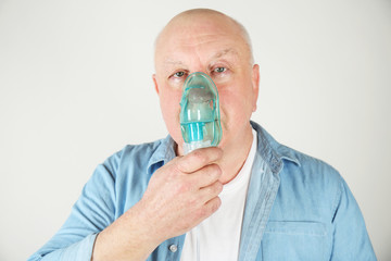 Senior man using asthma machine on light background