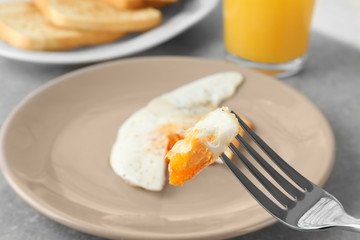 Fork with piece of over hard egg and plate on background