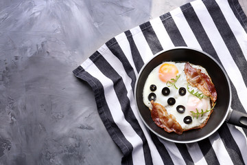 Delicious over hard eggs with bacon, olives and arugula in pan on kitchen table