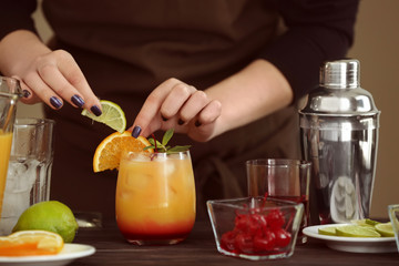 Woman decorating glass of Tequila Sunrise cocktail on kitchen table