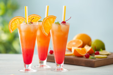 Glasses of Tequila Sunrise cocktail with citrus slices on wooden table