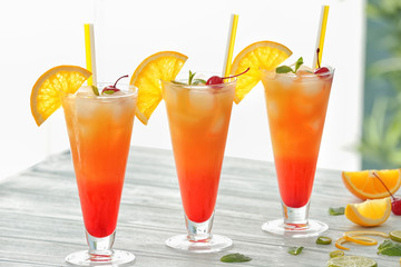 Glasses of Tequila Sunrise cocktail with citrus slices on wooden table