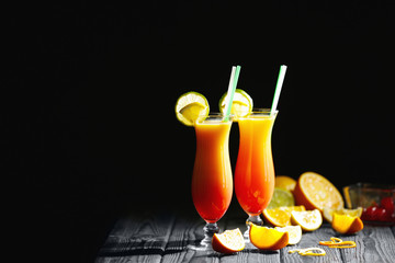 Glasses of Tequila Sunrise cocktail with citrus slices on dark background