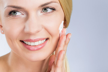 Obraz premium Happy woman applying cream on face looking away