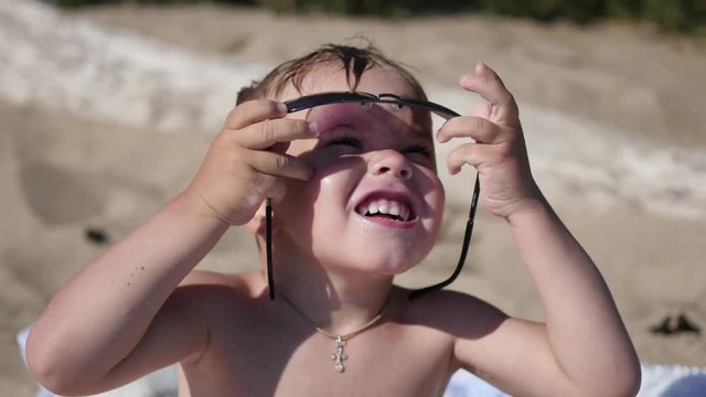 The child tries to wear sunglasses. The beach, a Sunny hot day