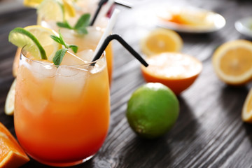 Glass of Tequila Sunrise cocktail with fruits on wooden table