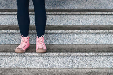 Fototapeta na wymiar Woman legs in black leggings and pink sneakers standing on a stone stage