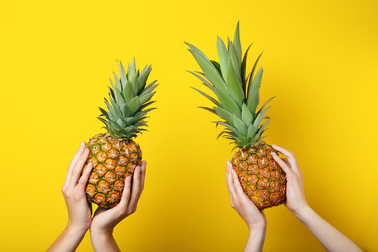Female hands holding ripe pineapples on yellow background
