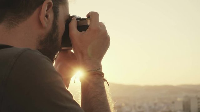 A young passionate photographer using a vintage film camera to photograph the city during sunset from a high angle