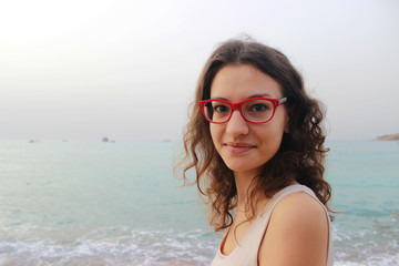Girl in red glasses on the coast on a cloudy day Vacation by the sea. Summer, outdoors. Beach landscape.
