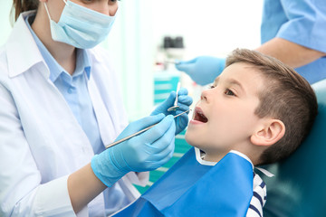 Dentist examining little boy's teeth in clinic