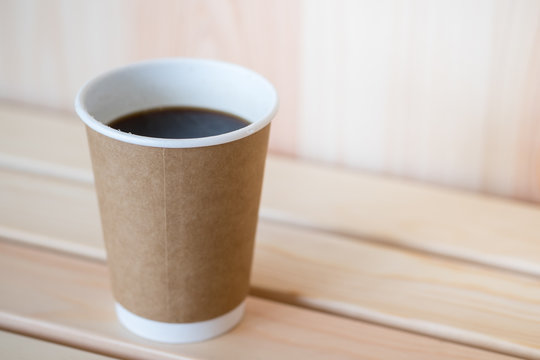 Close up of hot black coffee americano paper cup on on wooden table.